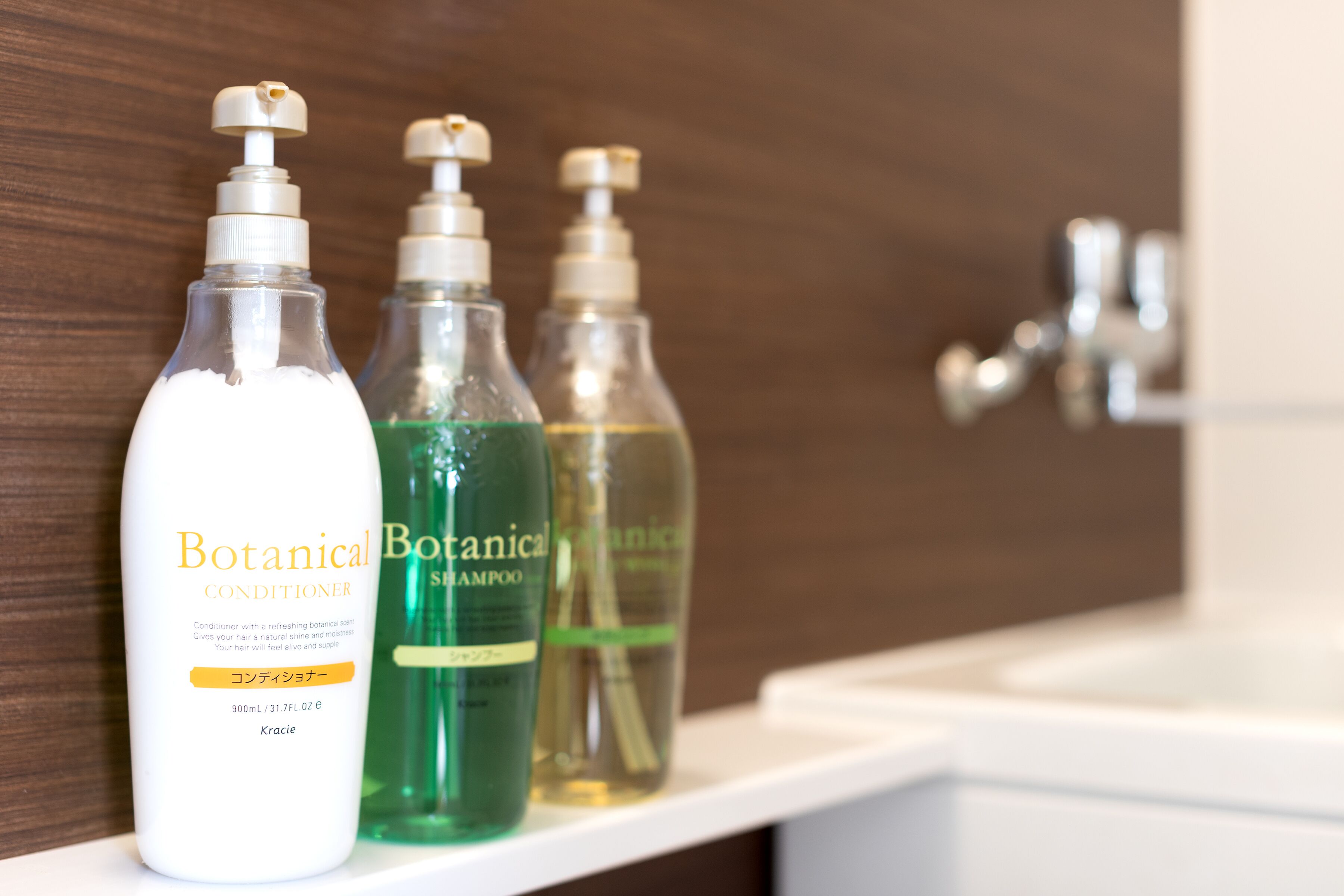 Three bottles of Botanical Conditioner and two bottles of shampoo on a white shelf in a bathroom.