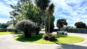 A parking lot with a white SUV parked near a palm tree and a large bush. - L'âme Voyageuse, Raffinée, 2-8 Pers, Plages à 15min (Baye)