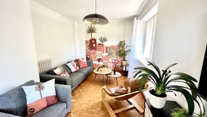 A modern living room with a grey sofa, a wooden coffee table, and a hanging chair. There is a cityscape mural on the wall and a large window on the right. - L'âme Voyageuse, Raffinée, 2-8 Pers, Plages à 15min (Baye)