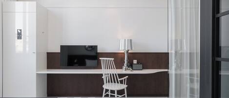 A modern hotel room with a bed, a desk, a chair, a TV, and a lamp.