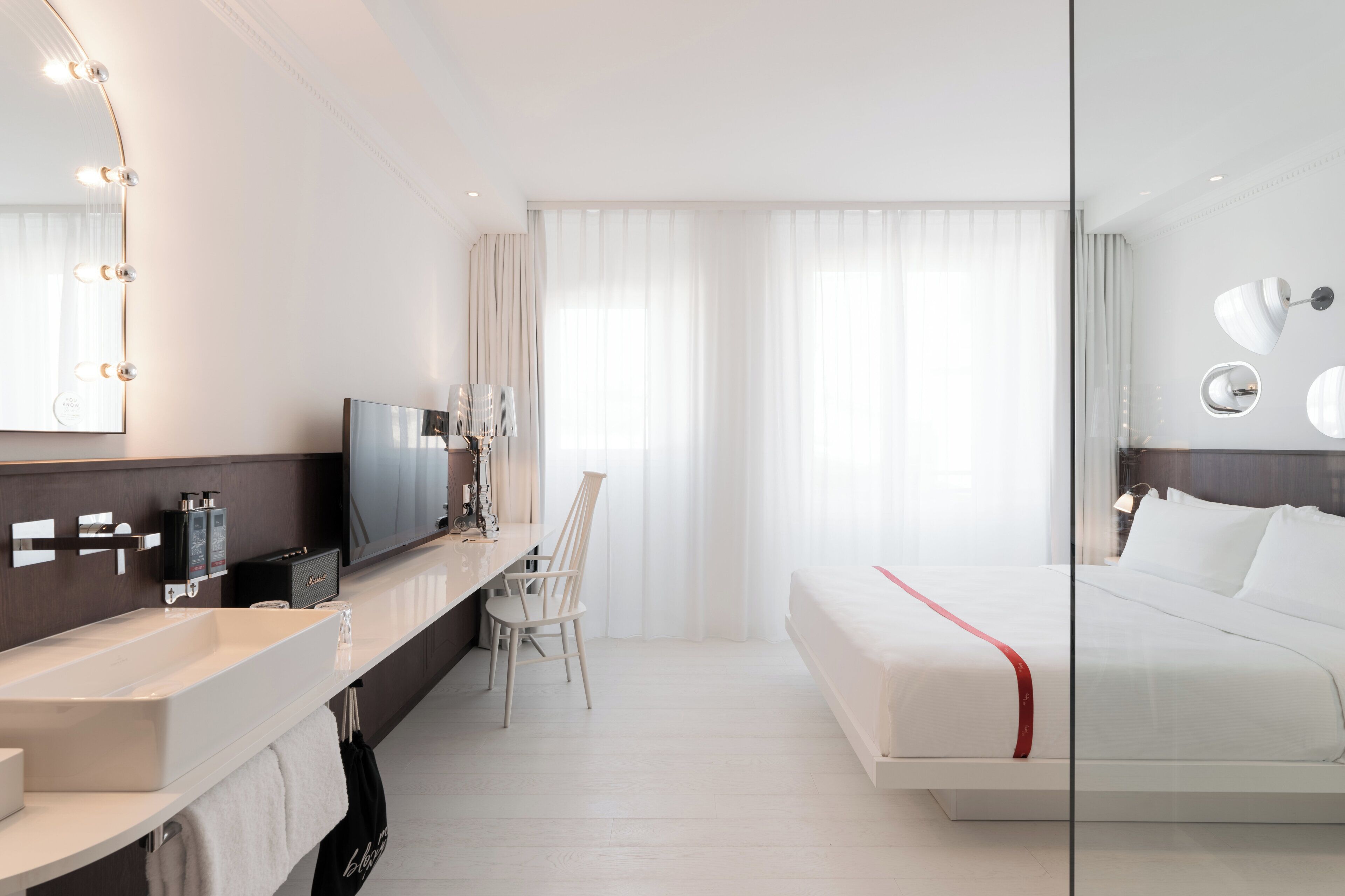 A modern hotel room with a large bed, a vanity with a mirror and lights, a television, and a desk with a chair.