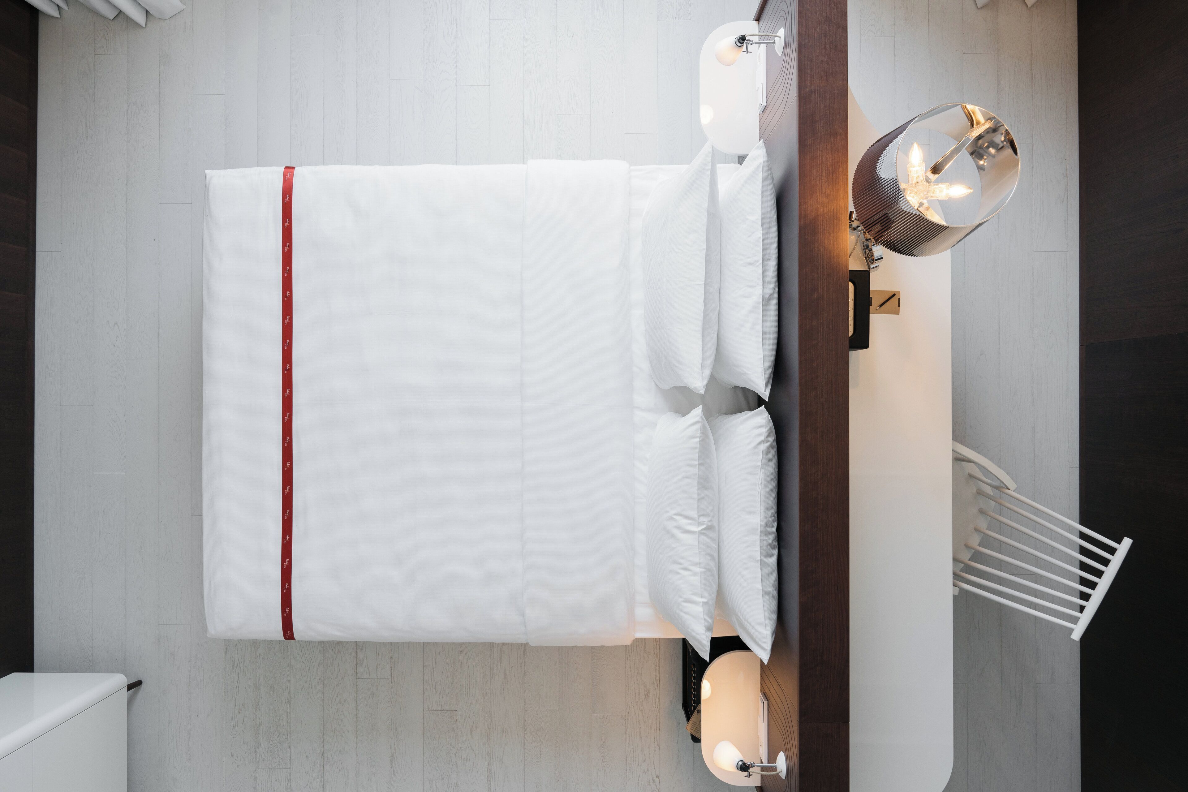 Una cama bien hecha con sábanas blancas y un borde rojo, un aplique de pared y un radiador blanco.