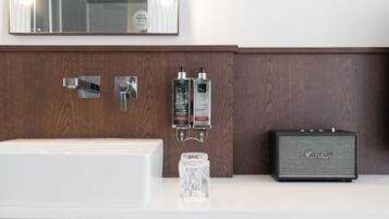 Un baño con tocador de madera, un lavabo blanco, dos botellas de jabón para manos, un vaso y un amplificador Marshall.