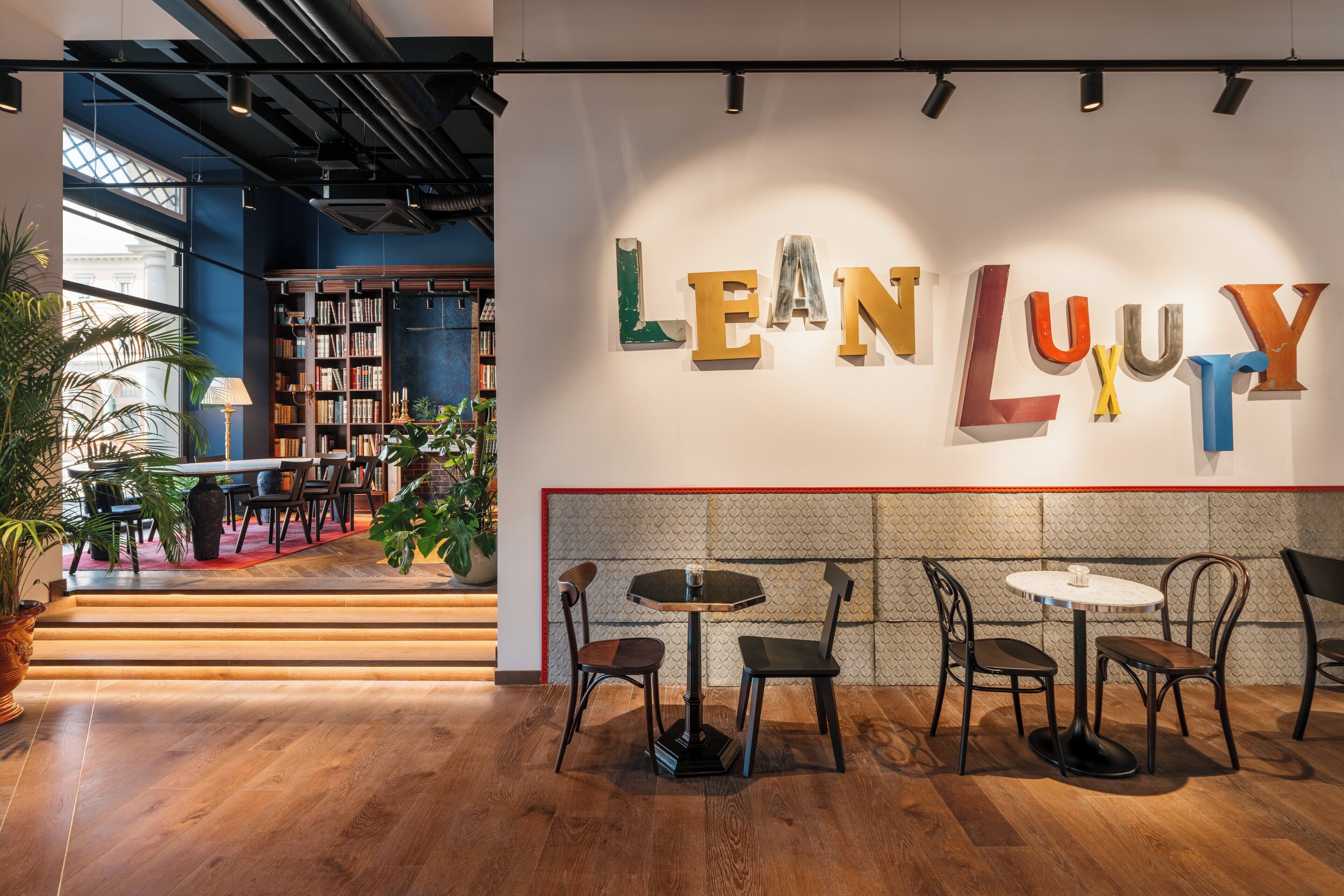 Un interior modern amb un rètol que diu 'LEAN LUXURY', terres de fusta i una zona d'estar amb taules i cadires.
