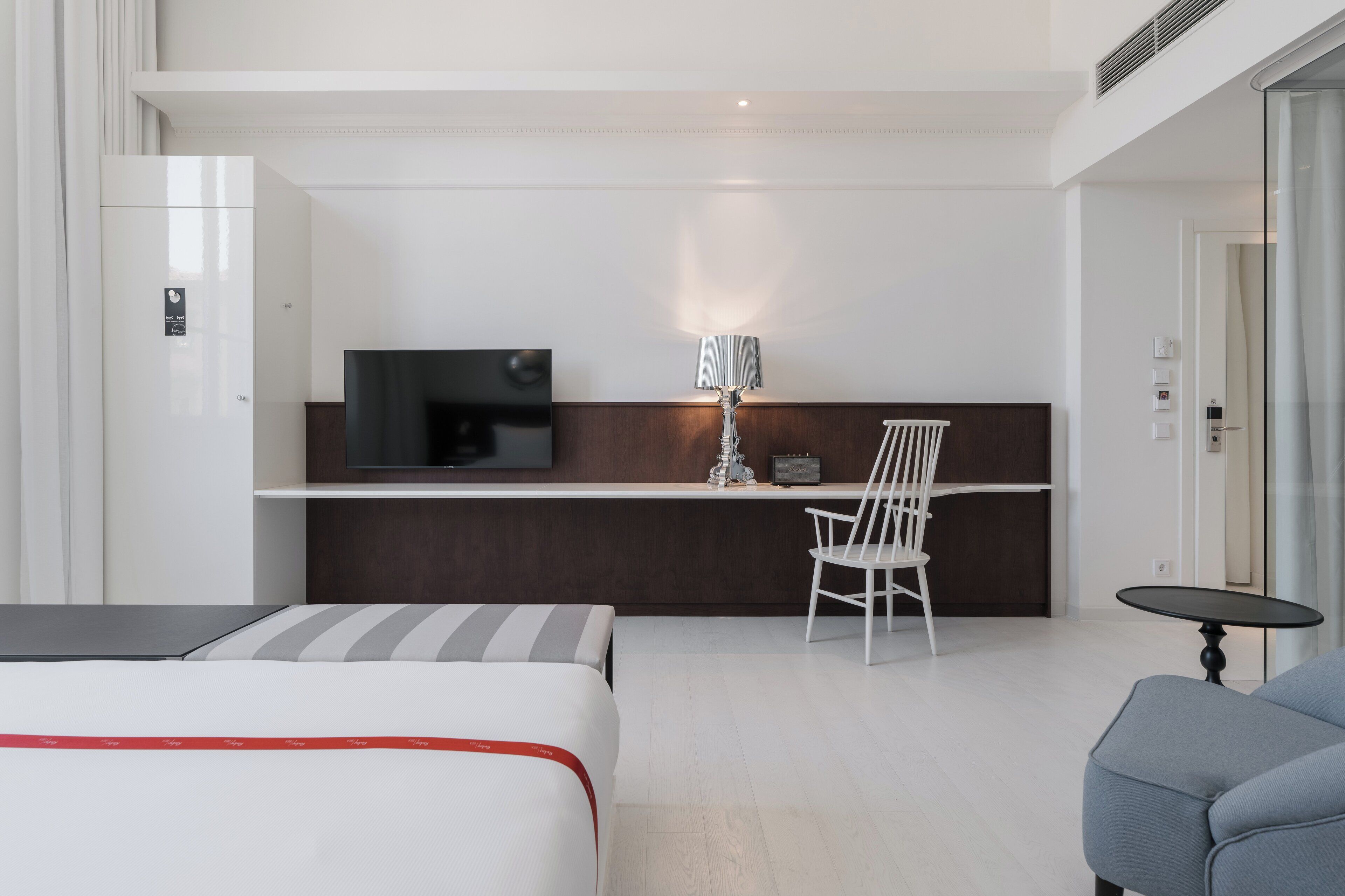 Ein modernes Hotelzimmer mit einem Bett, einem Schreibtisch mit Fernseher, einem Sessel, einer Lampe und einem kleinen Tisch.