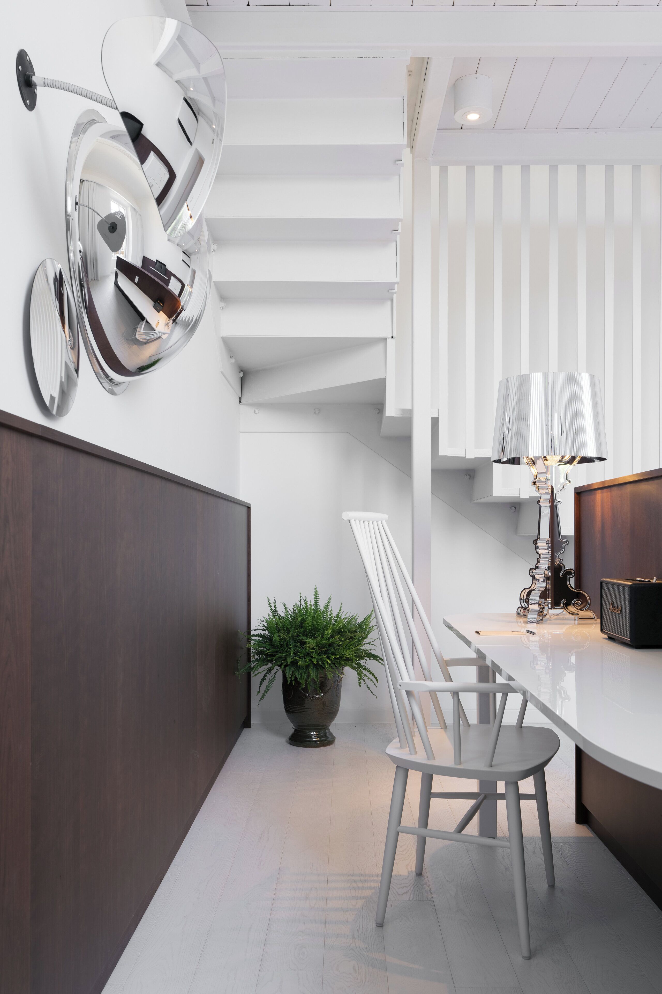A modern kitchen with a white countertop, a dining area with a white chair, and a potted plant.