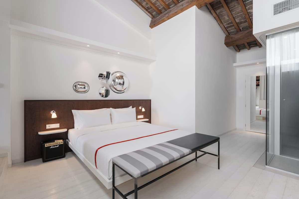 A modern bedroom with a large bed, bedside tables, a bench, and a wall-mounted light fixture.
