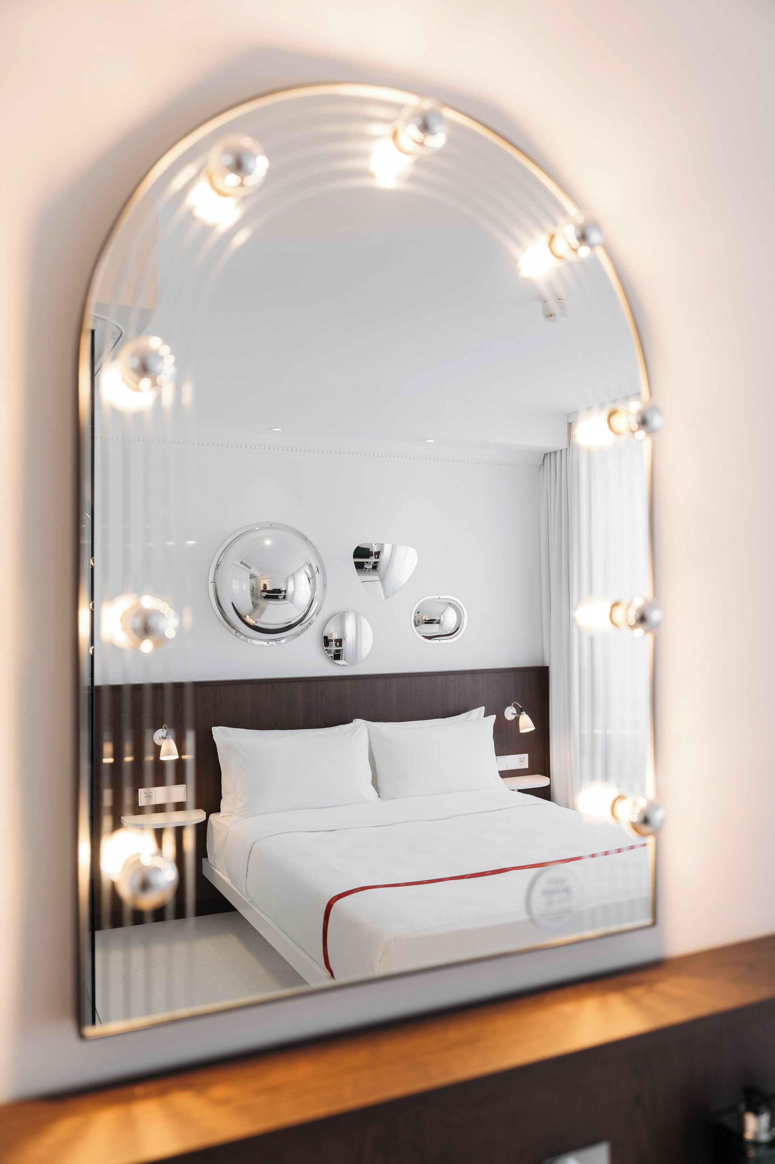 A hotel room with a large mirror, a bed, and wall-mounted lights.