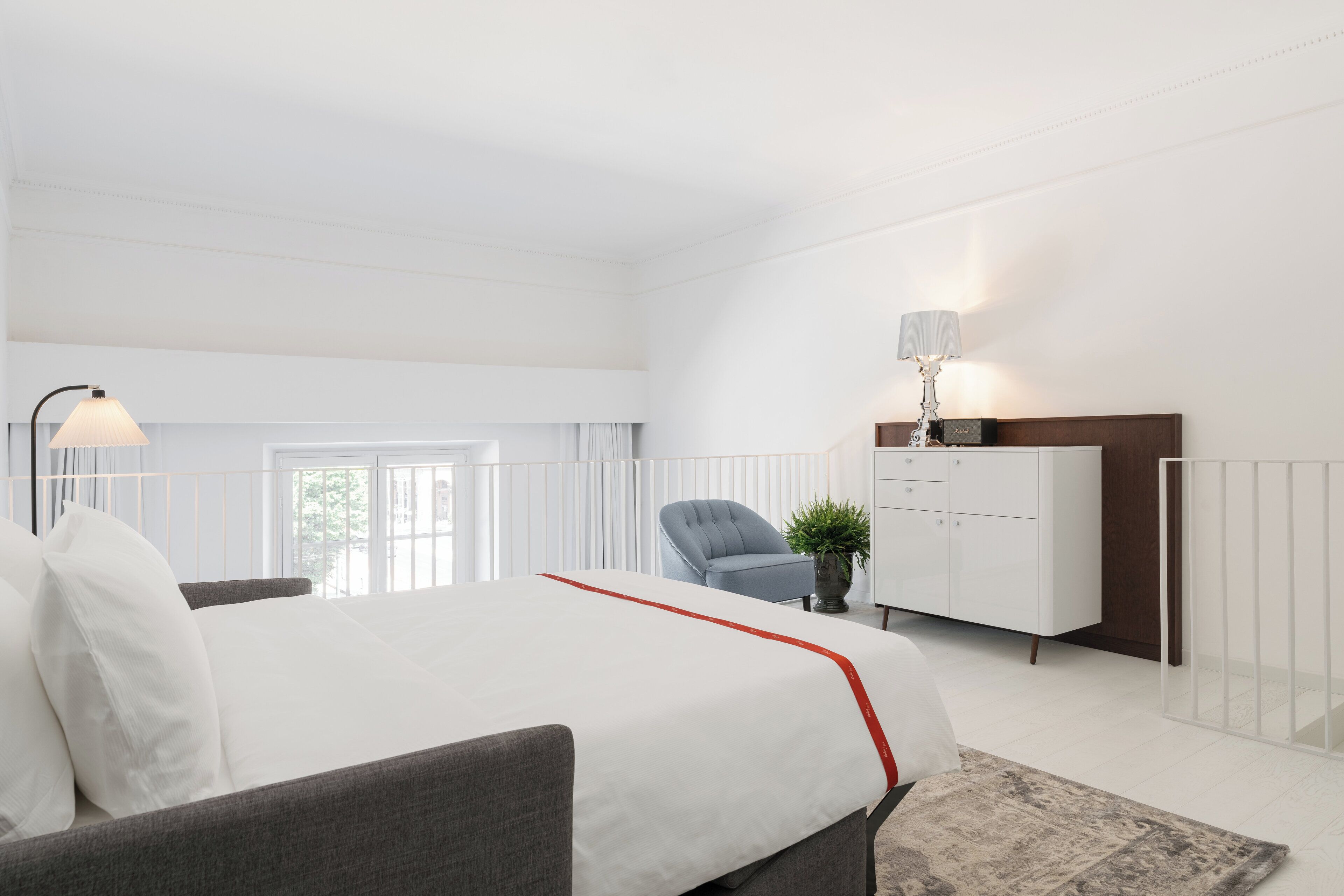 A modern bedroom with a large bed, a grey sofa, a white wardrobe, a desk, and a window with curtains.