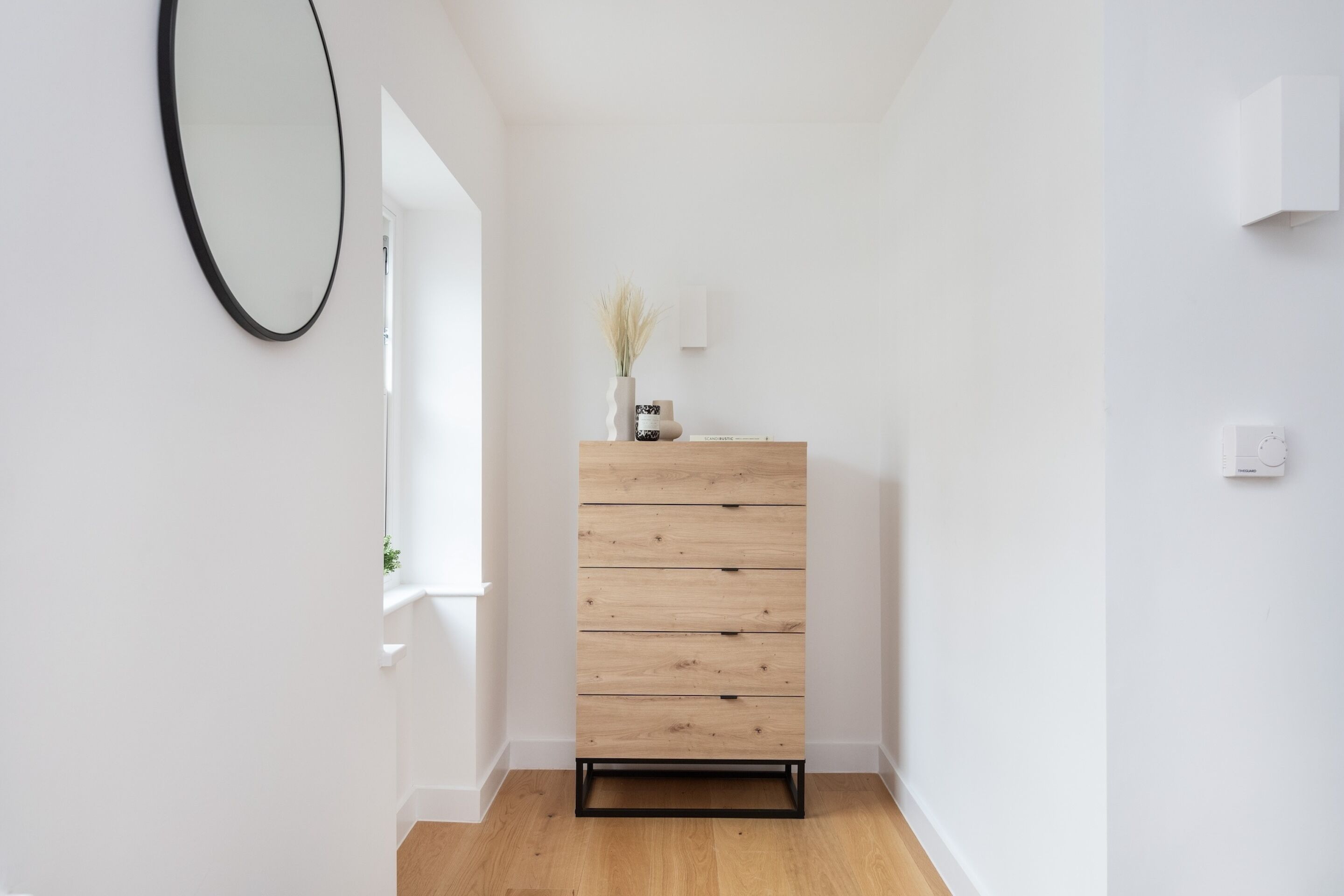 A minimalist room with a wooden dresser, a mirror, and a small plant on the dresser.