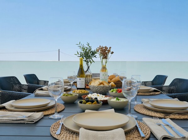 An outdoor dining setup with a table set for four, including plates, cutlery, glasses, and a bottle of wine. - Lilu Villa 1 With Private Pool and Seaview (Kos)