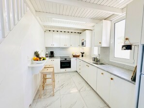 A modern kitchen with white cabinets, a marble floor, and a wooden stool. - Lilu Villa 1 With Private Pool and Seaview (Kos)
