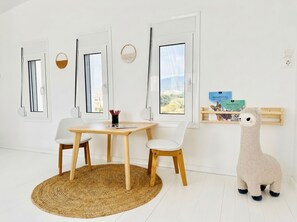 A room with a round woven rug, a wooden table, two white chairs, and a stuffed animal on a shelf. - Lilu Villa 1 With Private Pool and Seaview (Kos)
