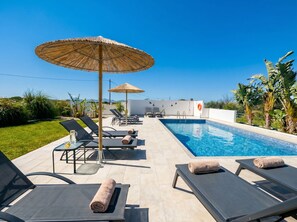 Un área junto a la piscina con sillas de descanso, piscina y sombrilla de paja.