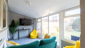 A bright room with a green sofa, yellow bean bag, and a TV on the wall.