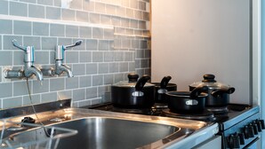 A kitchen with a stainless steel sink, two faucets, a stove, and two pots on the stove.