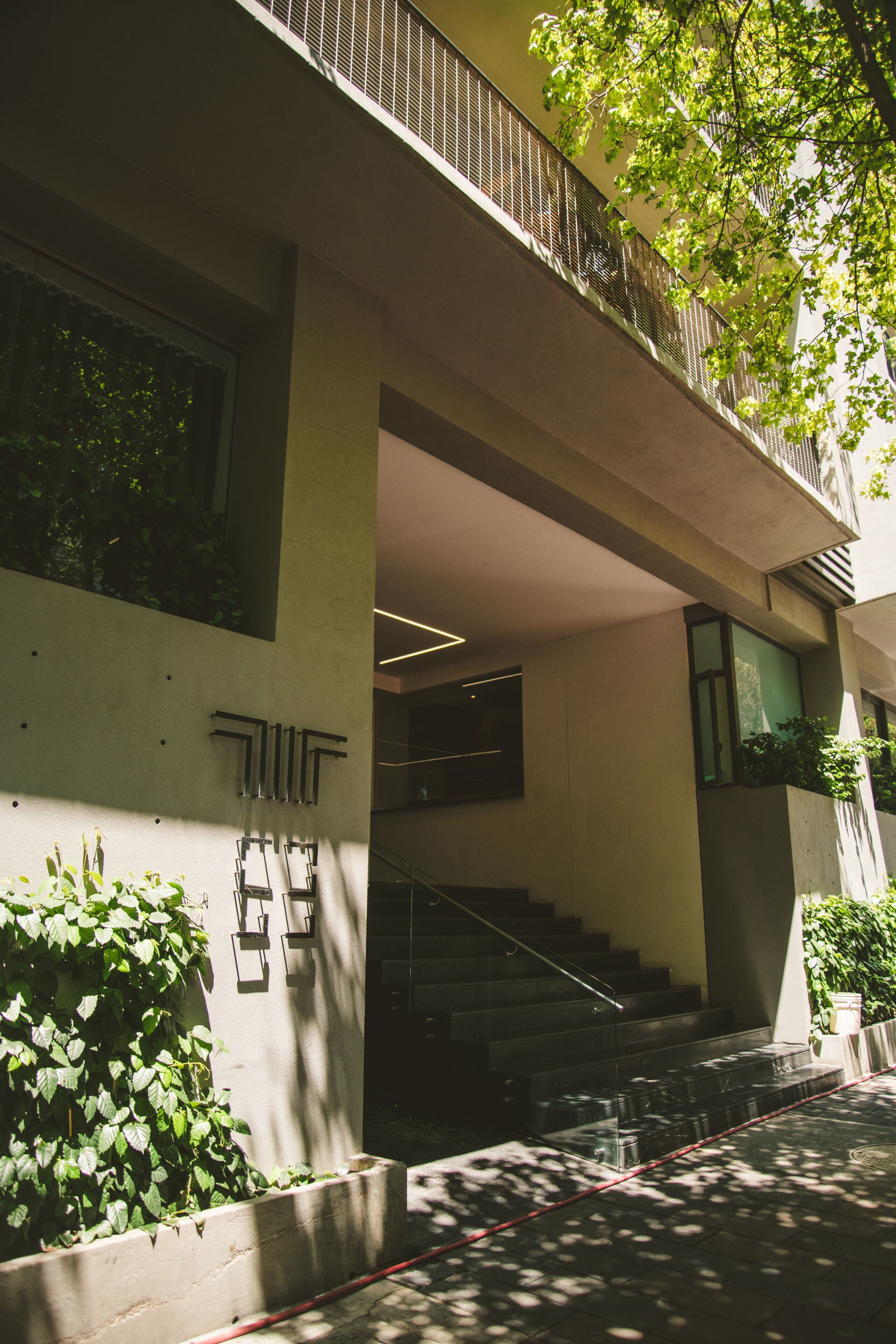 A modern building with a concrete facade, a set of stairs leading to an upper level, and a small garden area with greenery.