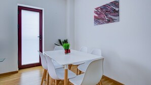 Ein Essbereich mit einem weißen Tisch und Stühlen, einer Tür mit rotem Rahmen und einem Gemälde an der Wand.