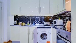 Eine kompakte Küche mit weißen Schränken, einer Waschmaschine, einer Mikrowelle und einem Toaster.