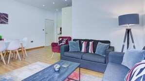 Ein modernes Wohnzimmer mit einem grauen Sofa, einem roten Sessel, einem Esstisch mit Stühlen und einer Stehlampe.