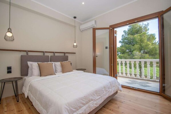 A bedroom with a large bed, a small table, two hanging lights, and a sliding glass door leading to an outdoor area.