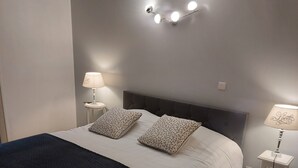 A neatly made bed with two pillows, a bedside lamp, and a wall-mounted light fixture. - Location en Savoie (Arith)