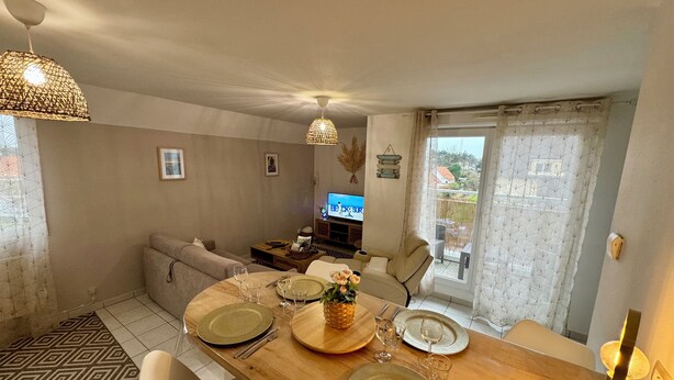 Un coin repas avec une table en bois dressée pour quatre personnes, un canapé, un téléviseur et une vue sur l’extérieur.