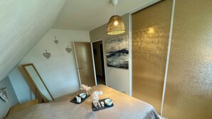 Une chambre à coucher comprenant un lit, une table de chevet, un luminaire suspendu, une porte et un mur à la finition texturée.