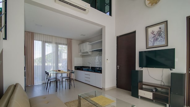 A modern living room with a sofa, a glass coffee table, a TV, and a kitchen area in the background. - Casa de Lily (Tabanan)