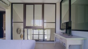 A hotel room with a bed, a desk, a TV, and a sliding glass door leading to a balcony. - Casa de Lily (Tabanan)