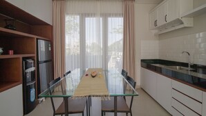 A modern kitchen with a glass dining table, white cabinets, and a stainless steel sink. - Casa de Lily (Tabanan)