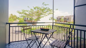 A covered balcony with a table and chairs, a tiled floor, and a view of buildings and trees. - Casa de Lily (Tabanan)