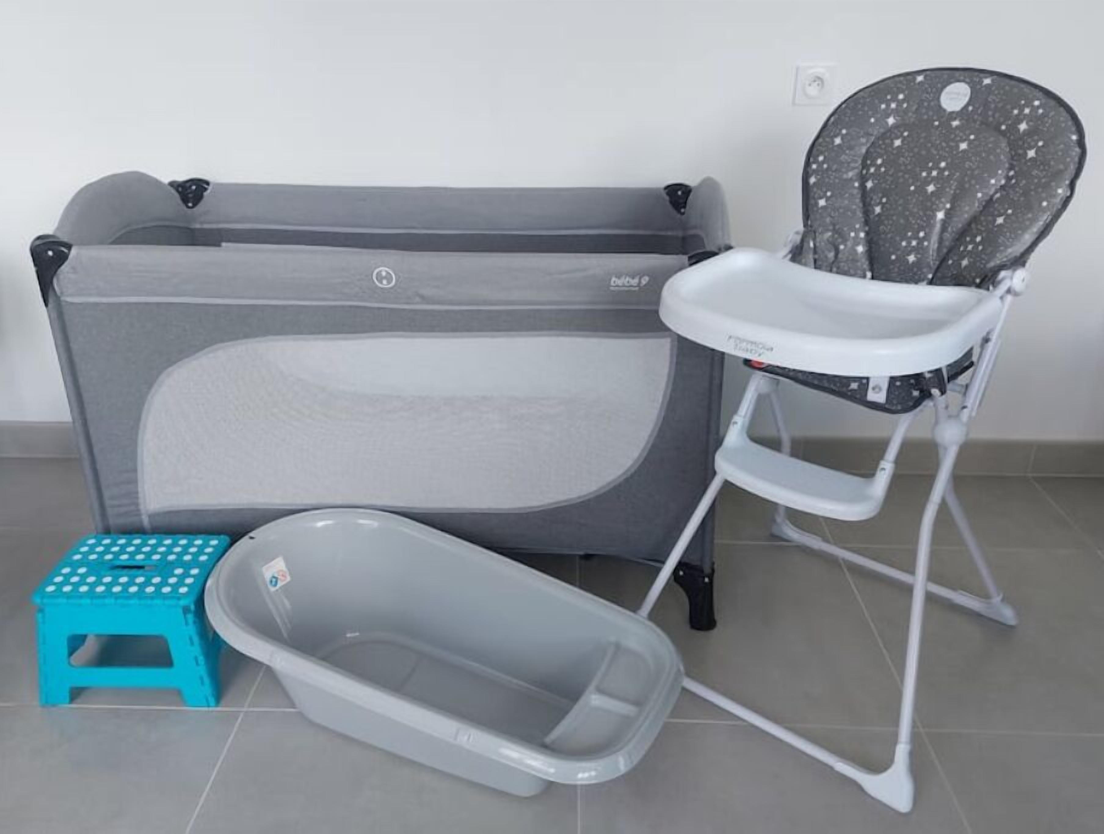 A baby changing station with a grey changing table, a grey baby seat, a blue stool, and a grey baby bathtub.