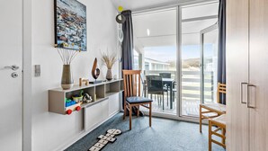 Een moderne woonkamer met een groot raam, een houten stoel, een kleine tafel en een decoratieve plank met diverse objecten.