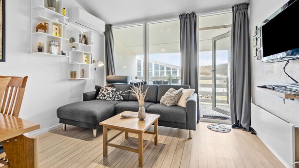 Een moderne woonkamer met een grijze bank, een houten salontafel en een aan de muur bevestigde televisie.