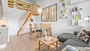 Een moderne woonkamer met een houten trap, een eethoek met stoelen en een tafel, en een grijze bank met decoratieve kussens.