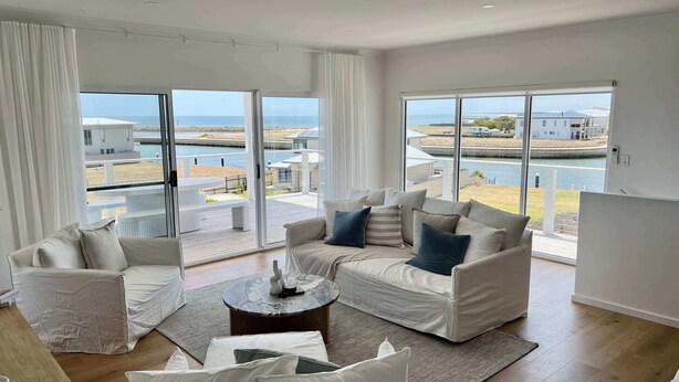 A spacious living room with a large sliding glass door leading to a balcony with a view of the sea and buildings. - Casa Bianca - Ocean and harbour views (Cape Jaffa)