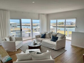 Amplio salón con un gran ventanal corredera que da a un balcón con vistas al mar y edificios.