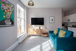 A modern living room with a teal sofa, a flat-screen TV, and a large window.