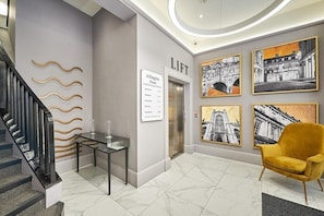 A hotel lobby with a staircase, an elevator, a reception desk, and artwork on the walls.