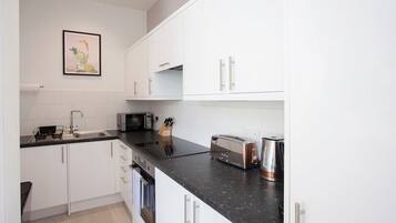 A modern kitchen with white cabinets, a black countertop, and stainless steel appliances including a toaster and kettle.