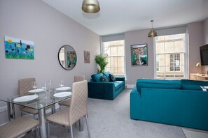 A modern living room with a glass dining table, teal sofas, and artwork on the walls. - Stunning Apt - Centre of Historic Bath (Bath)