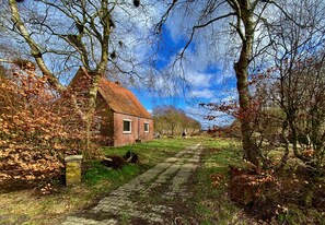 Entorno rural con una casa de ladrillo, un camino adoquinado y árboles cubiertos de hojas.