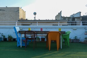 A patio area with a table and chairs, surrounded by potted plants and a white wall.