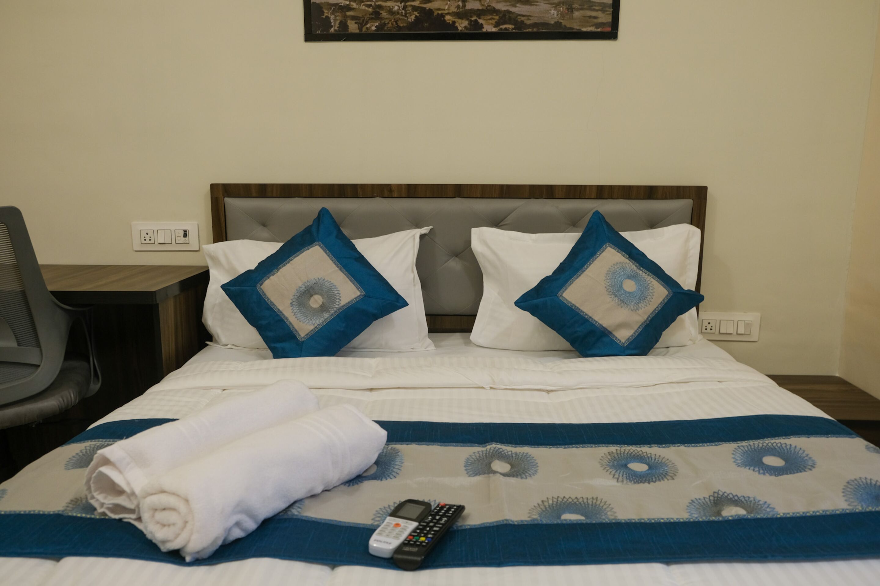 Ein ordentlich bezogenes Bett mit einer blau-weißen Tagesdecke, zwei Kissen mit blau-weißen Mustern und einer Fernbedienung darauf.