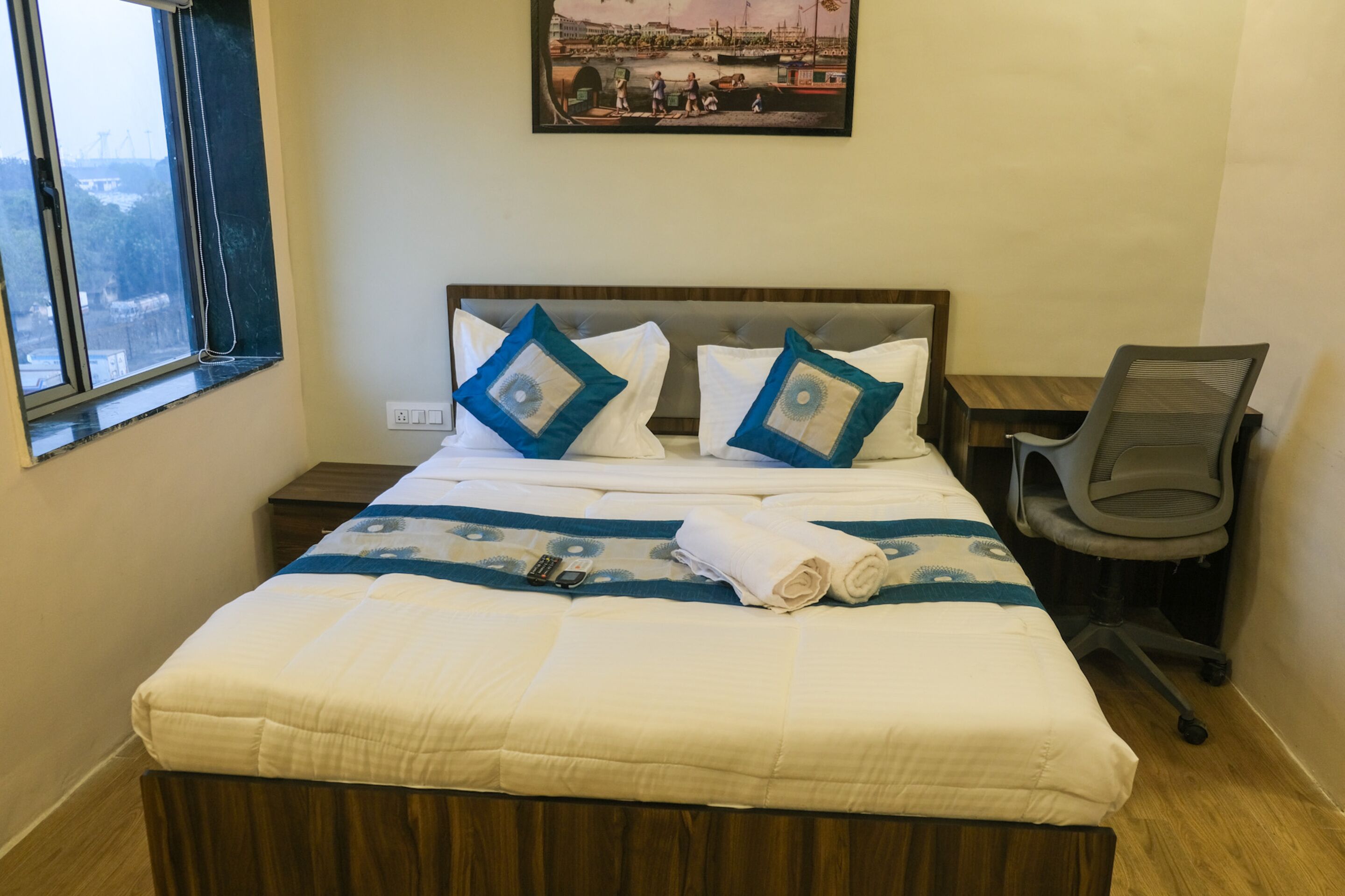 Une chambre d’hôtel avec un lit, une chaise, un tableau au mur et une fenêtre.