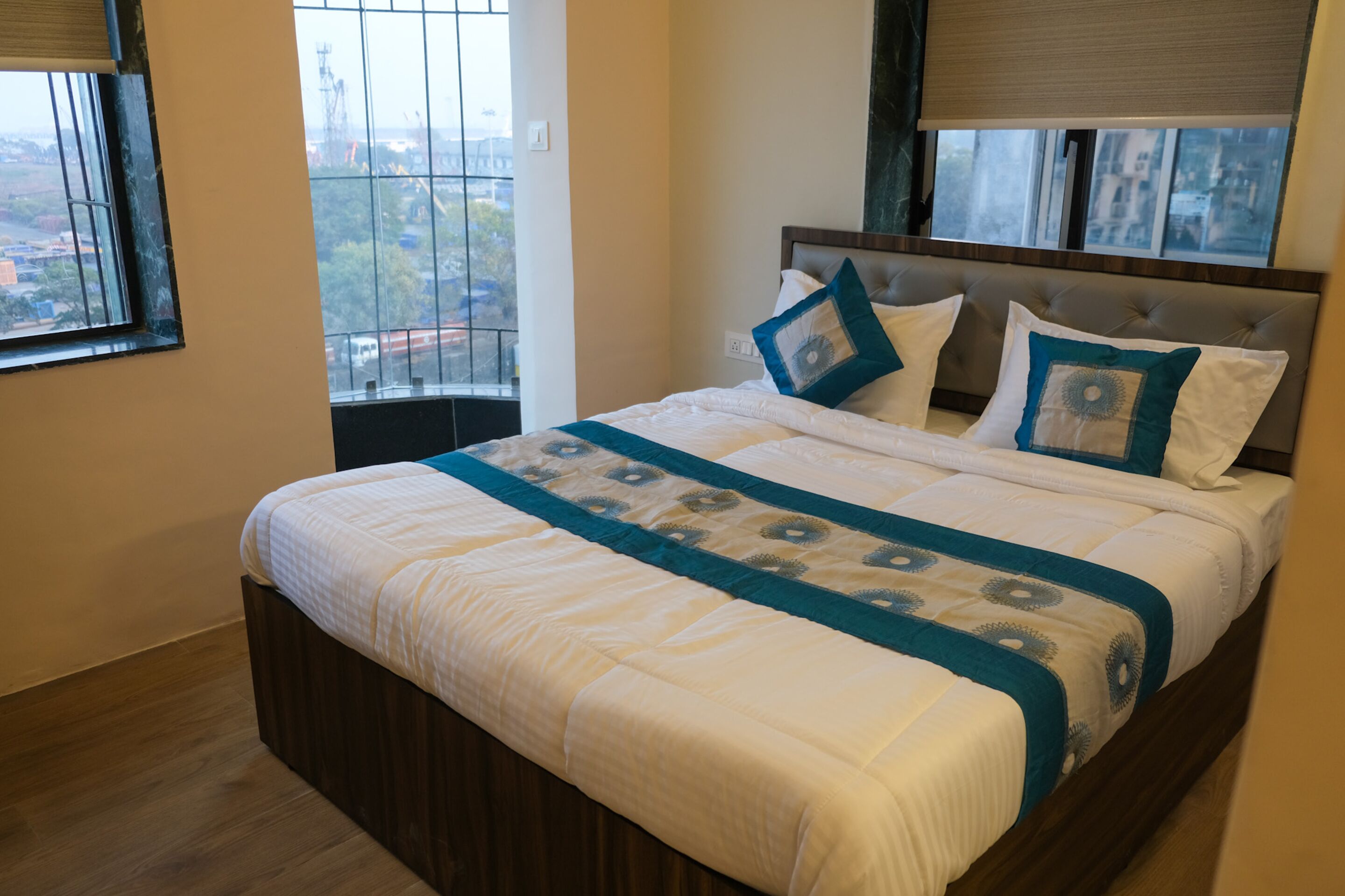 A bedroom with a large bed, a window with blinds, and a view of buildings outside.