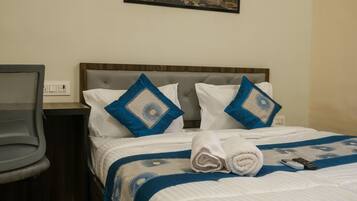 Una cama bien tendida con un edredón azul y blanco, dos almohadas con diseños azules y blancos, una toalla blanca enrollada y un control remoto sobre la cama.