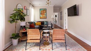 A living room with a sofa, two wicker chairs, a coffee table, a floor lamp, and a painting on the wall. - Large Home w/ Back Yard Oasis | Perfect for Groups (New Orleans)