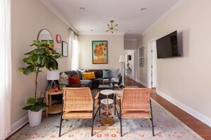 A living room with a sofa, two wicker chairs, a coffee table, a floor lamp, and a painting on the wall.